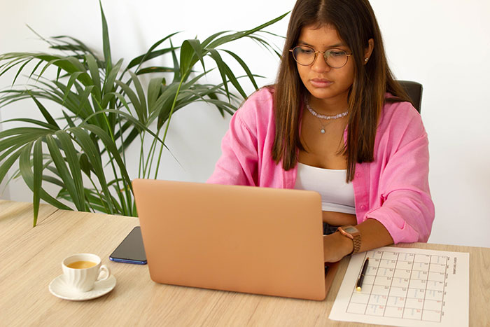 female typing on laptop with coffee cup on table