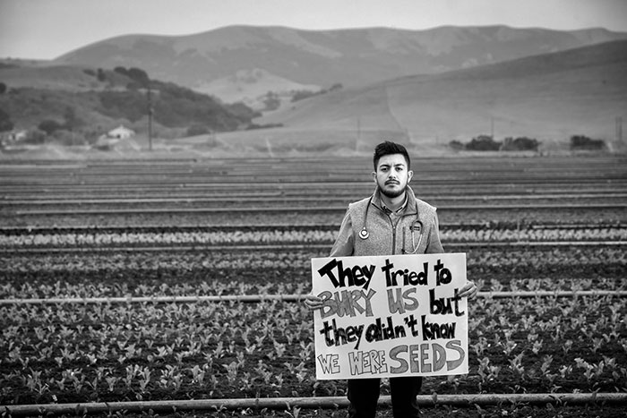Latinx man standing with sign in with agricultural field in background