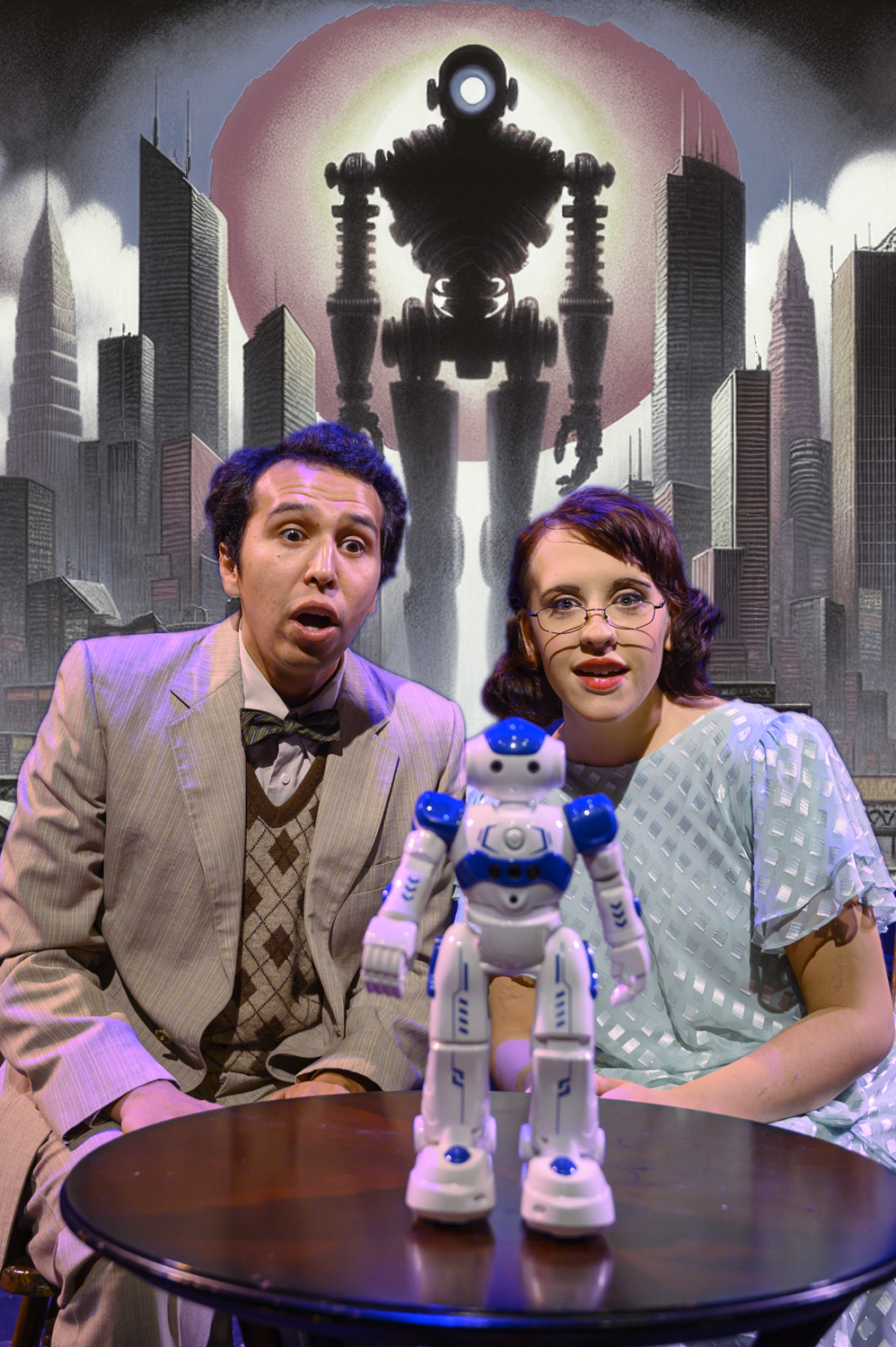 Two actors sit at a small table, reacting in surprise as a small white and blue robot stands in front of them, with a large shadowy robot and a futuristic cityscape projected behind them.